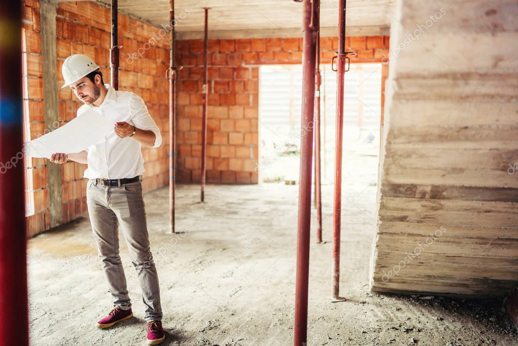 male engineer working on construction site, inside interior brick walls wearing hard hat and reading plans
