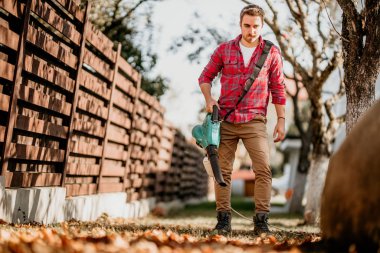 Portre yakışıklı bahçıvan Bahçe üfleyici ve vakum kullanarak. Ev bahçe ayrıntıları