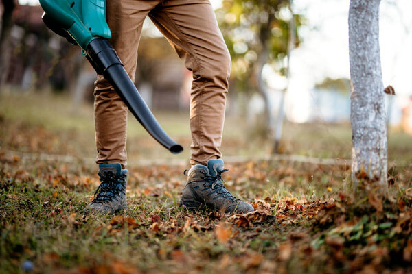 Close up details of leaves blowing, man using multiple tools while working in garden