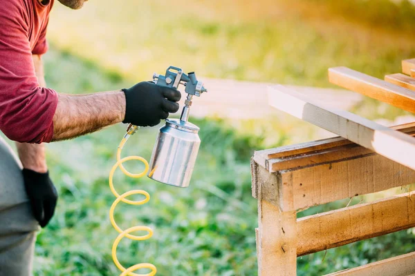 industrial worker using paint gun or spray gun for applying paint on brown timber wood
