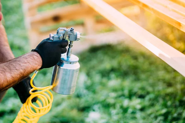 Industrial male worker painting brown timber using spray gun and air compressor