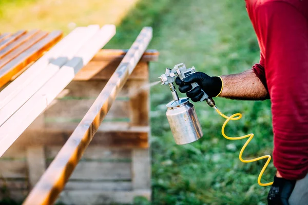 Industrial carpenter painting timber with spraygun, outdoors