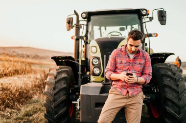 Çiftçi hasat akıllı telefon ve traktör kullanarak portresi. Modern tarım makineleri kavramı ile 