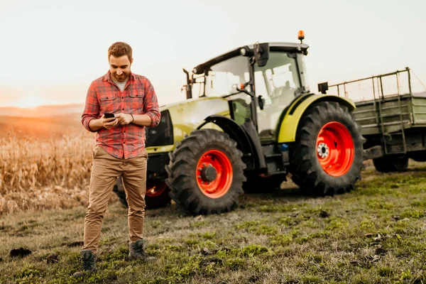 现代农业中使用智能手机在田间劳动的男性农民 拖拉机背景 — 图库照片