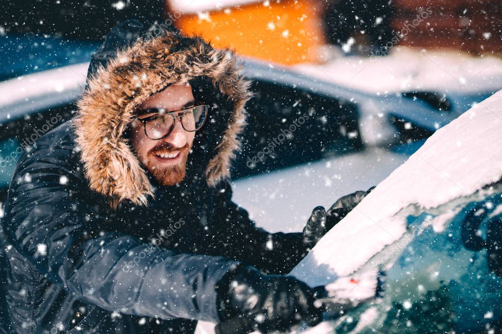 close up portrait of man removing snow from car. Caucasian man cleaning car windsheld during snowfall