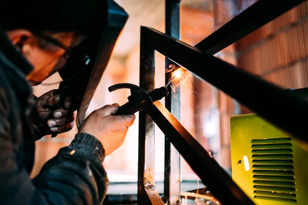 Soldador em uniforme de proteção e máscara de soldagem tubo de metal no local industrial — Fotografia de Stock