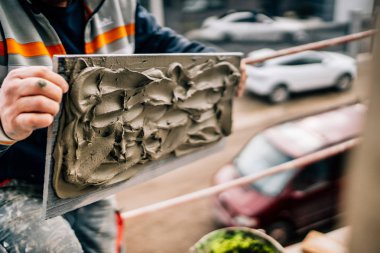 Şantiyede mimari cepheye yapıştırıcılı mermer taş yerleştiren sanayi işçisi. Şantiyedeki kişiler