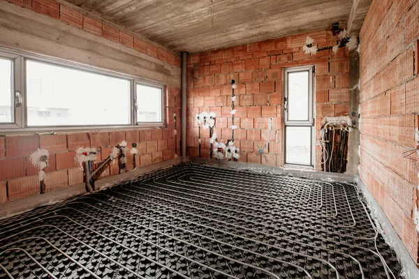 Radiant underfloor heating installation with flexible tubing mounted on construction site. Electrical wires and tubes in building site