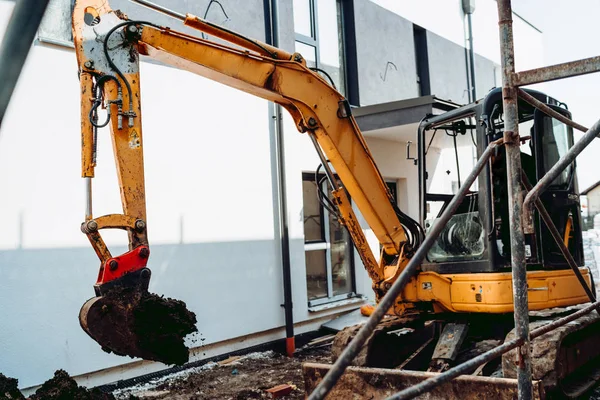 Mini excavator moving earth and digging at new house construction site