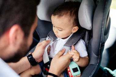 Portrait of young father securing baby in child seat of car clipart