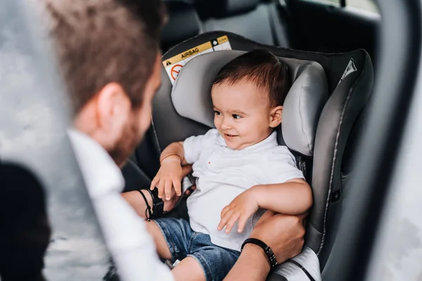 Father putting one year old baby in child car seat and smiling. Lifestyle concept