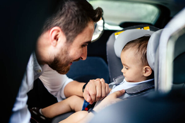 Smiling baby in child car seat going for a family roadtrip.Father fasten Safety seatbelt