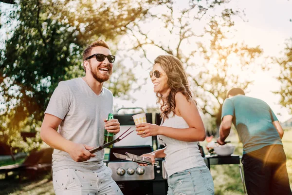 Grupo de amigos sorridentes em férias tomando cervejas e cozinhar no churrasco do jardim. Estilo de vida, conceito de lazer — Fotografia de Stock