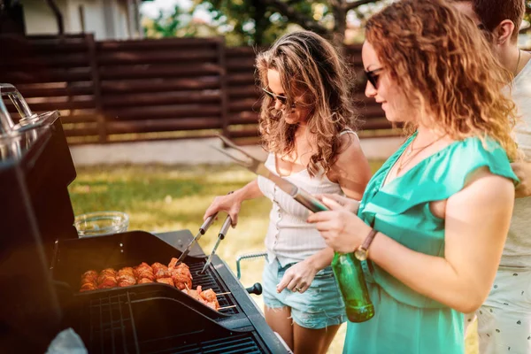 Amerikalı kızlar arkadaşları ile bir arka bahçesinde barbekü parti, gülerek ve yemek yaparken gülümseyerek sahip — Stok fotoğraf
