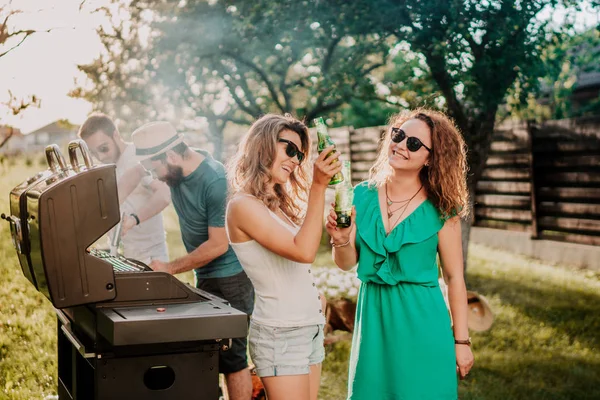 Friends having a barbecue party, girls laughing and smiling, drinking and cooking