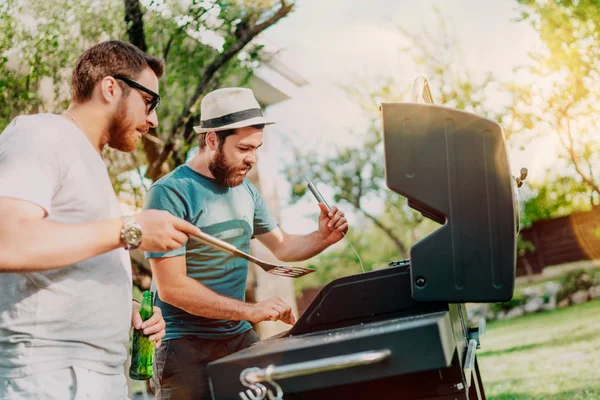 Dois amigos cozinhando na grelha durante o verão. Retrato de homens grelhando e fazendo uma festa de churrasco no jardim — Fotografia de Stock