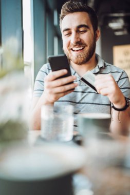 Yerel kafede akıllı telefon ve kredi kartı kullanan gülümseyen adamın portresi. kredi kartı ile online alışveriş 