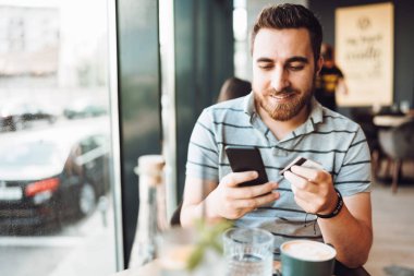 yakışıklı adam kredi kartı kullanarak akıllı telefon bir ödeme yapıyor. Mobil alışveriş konsepti