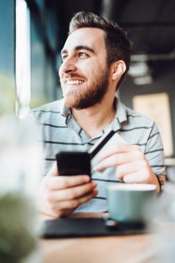 kredi kartı ile online alışveriş yaparken yerel kafede akıllı telefon ve kredi kartı kullanan adam 