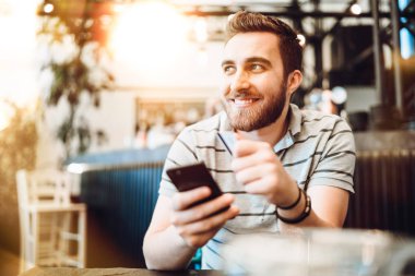 Kredi kartı ve cep telefonuyla ödeme yapan adam. Modern ödeme sy