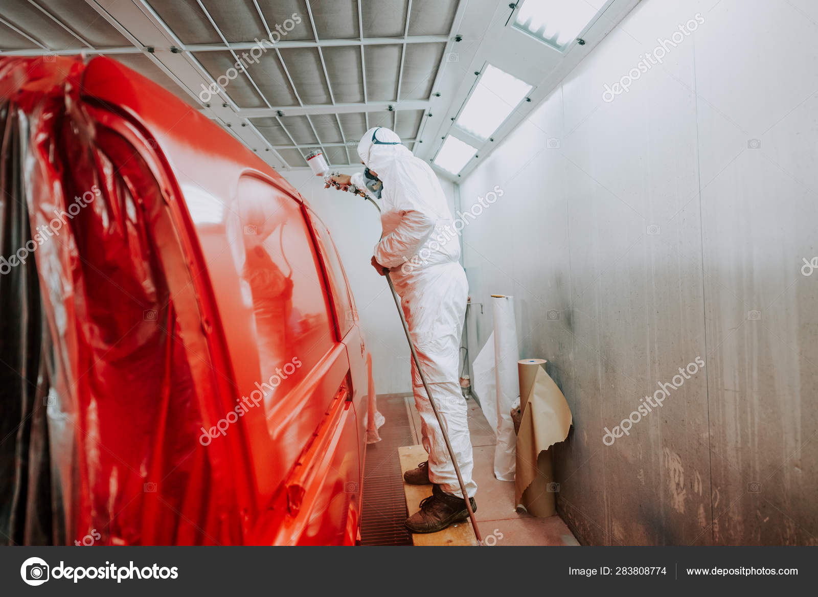 Worker painting a red car in a special garage, wearing a white costume