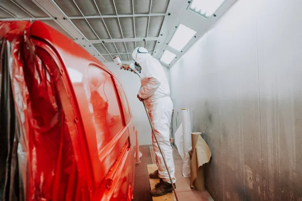 Trabajador pintando un coche rojo en un garaje especial, con un traje blanco —  Fotos de Stock
