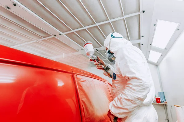 Detalhes da indústria automotiva - close-up de pintor aplicando tinta vermelha em um carro vermelho vestindo roupas de proteção — Fotografia de Stock