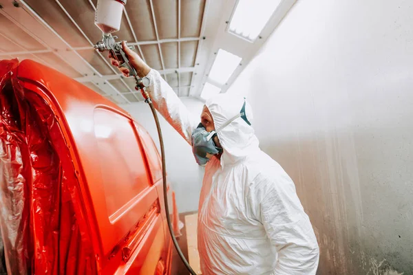İşçi bir airbrush gu kullanarak oto garajında kırmızı bir multivan veya araba boyama — Stok fotoğraf