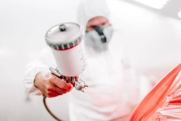 Porträt eines Arbeiters der Automobilindustrie mit einer Spritzpistole mit roter Farbe, der ein Auto in einer speziellen Kabine lackiert — Stockfoto