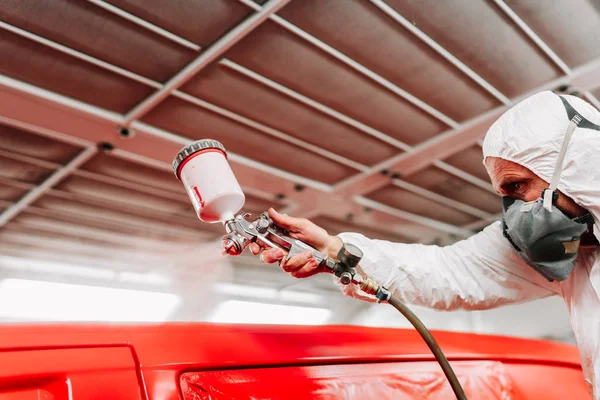 車のエンジニアと自動車整備士は、スプレーガンとコンプレッサーを使用して赤い車を作業し、塗装 — ストック写真