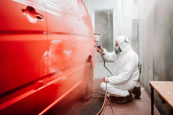 Автомеханик, работающий в автомобилестроении и покрашивающий красный фургон в специальный стенд — стоковое фото