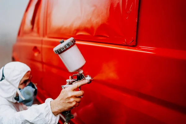 Работник покрасил красную машину в специальном гараже, одетый в полный костюм — стоковое фото