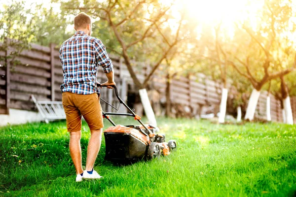 Портрет человека, стригущего траву в саду с помощью газонокосилки с бензиновым двигателем — стоковое фото