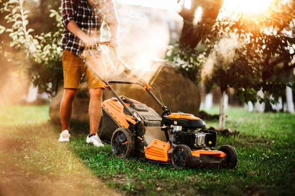 Jardinier utilisant tondeuse à gazon industrielle pendant le coucher du soleil d'été. Détails de l'aménagement paysager et du jardinage . — Photo