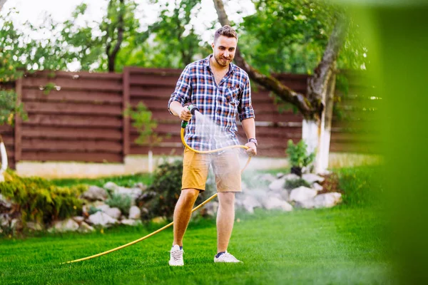 Uomo caucasico che lavora all'irrigazione dell'erba. Tubo sistema manuale, irrigazione del prato — Foto Stock