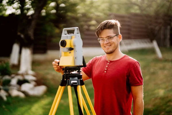 Retrato del topógrafo ingeniero caucásico que trabaja con la estación total en el proyecto de paisajismo —  Fotos de Stock