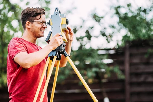 Porträtt av leende lantmätare arbeta med totalstation i trädgården — Stockfoto