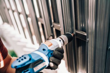 Tamirci, vidaları metal çitlere tutturmak için elektrik kablosu tornavida kullanıyor.