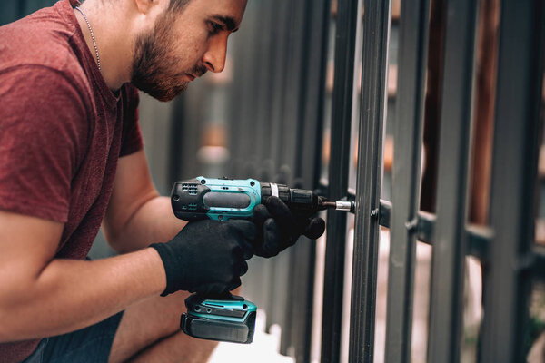 Close up of construction worker using screwdriver and drilling screws into metal fence