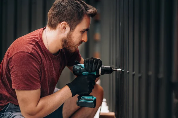 Handyman met accuschroevendraaier en boorschroeven in metalen hek — Stockfoto