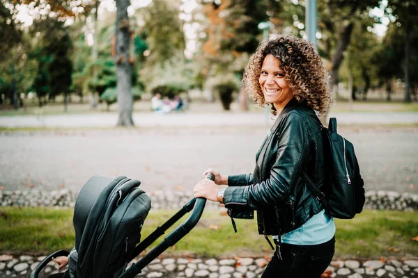 Młoda matka uśmiechnięta spacerując z wózkiem dziecięcym w parku. Szczegóły dotyczące macierzyństwa — Zdjęcie stockowe