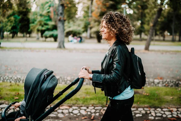 Tânără mamă plimbându-și copilul în parcul orașului cu o pra frumoasă — Fotografie, imagine de stoc