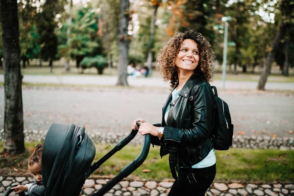 Portretul mamei fericite cărucior de mers pe jos în parc. Curly păr tânără mamă mers pe jos copil în parc — Fotografie, imagine de stoc