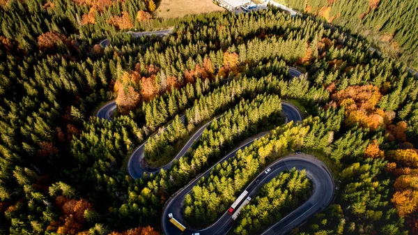 Beautiful drone view of winding forest road in the middle of mountains. Colourful landscape with rural road, trees with yellow leaves.