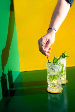 Mojito alkollü kokteyl ve barmen eli renkli arka planda buz karıştırıyor. Yeni modern kakaolar içki tasarımı konsepti