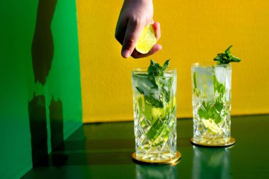 Mojito alkollü kokteyl ve barmen eli renkli arka planda limon sıkıyor. Yeni modern kakaolar içki tasarımı konsepti