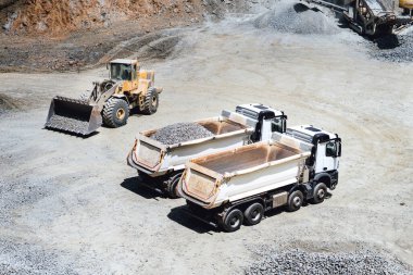 wheel loader working on site and loading dumper trucks. Heavy duty machinery working on construction site clipart