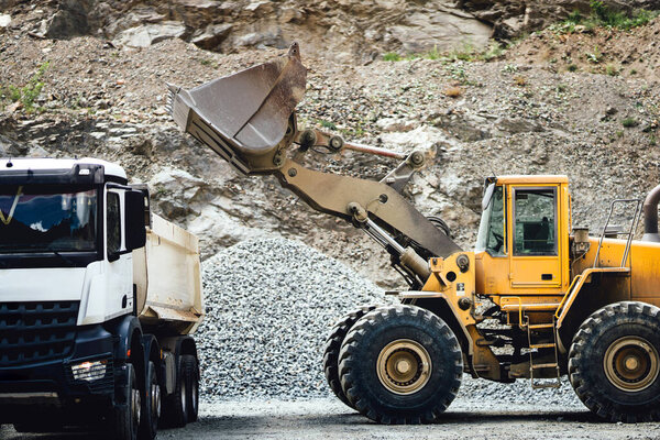 Крупные детали колесного погрузчика с совок, работающих на строительной площадке и погрузки гравия на самосвалы. Тяжелый бульдозер работает