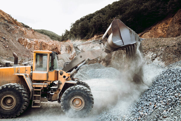 Industrial heavy duty wheel loader moving gravel on construction site. Multiple industrial machinery on construction site