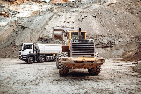Wheel loader bulldozer with blade loading dumper trucks on construction site